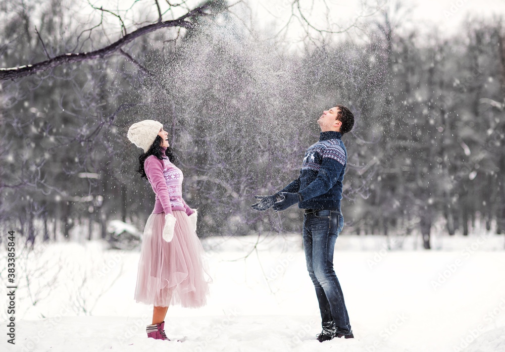Outdoors romantic portrait of happy attractive couple in love. They throwing snow in the air. Smiling and enjoying snowy weather. Wearing knitted hat, mittens and sweaters. Love concept. Valentine day