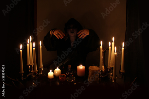 Fotografija Female Fortuneteller conjures in a dark room, candles are burning on a round eso