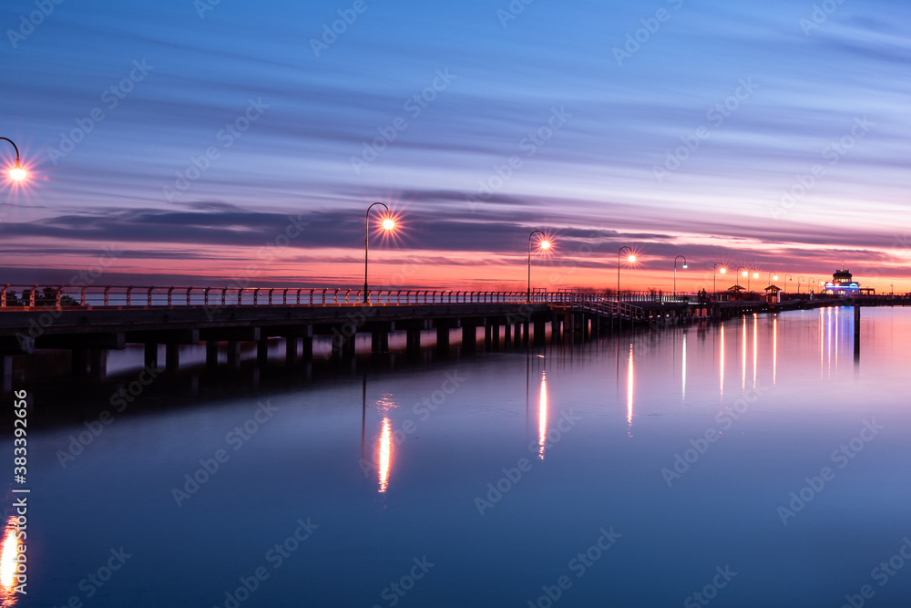 Long exposure of St Kilda Pier in Melbourne with lights on the jetty during sunset / blue hour with smooth water