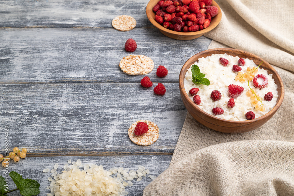 Rice flakes porridge with milk and strawberry in wooden bowl on gray wooden background. Side view, copy space. Rice flakes porridge with milk and strawberry in wooden bowl on gray wooden background. Side view, copy space.