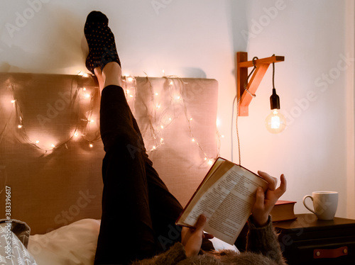 Pasando una tarde de otoño leyendo y descansando. Mujer adulta leyendo un viejo libro cómodamente acostada en una cálida y confortable habitación iluminada tenuemente photo