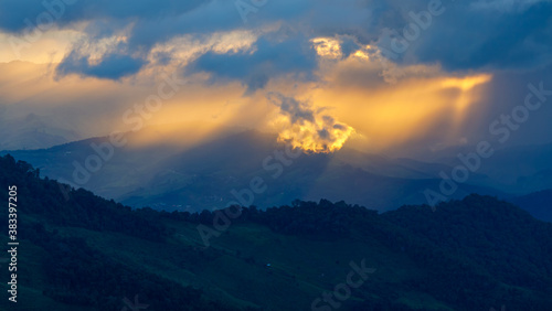 The sun shines through the clouds on the mountain top in the rainy season.