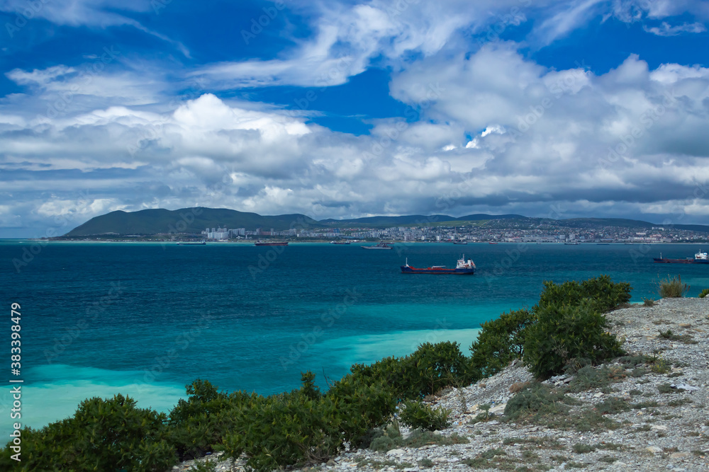 Blue sea with cargo ships against the blue cloudy sky, in the background of the city. View from the cliff