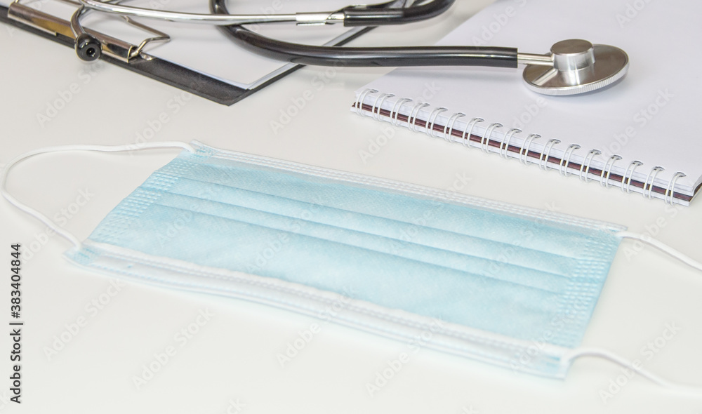 Close - up of the doctor's desktop with a medical mask, documents and a stethoscope on a white background, prevention of viral diseases, banner Close - up of the doctor's desktop with a medical mask, documents and a stethoscope on a white background, prevention of viral diseases, banner