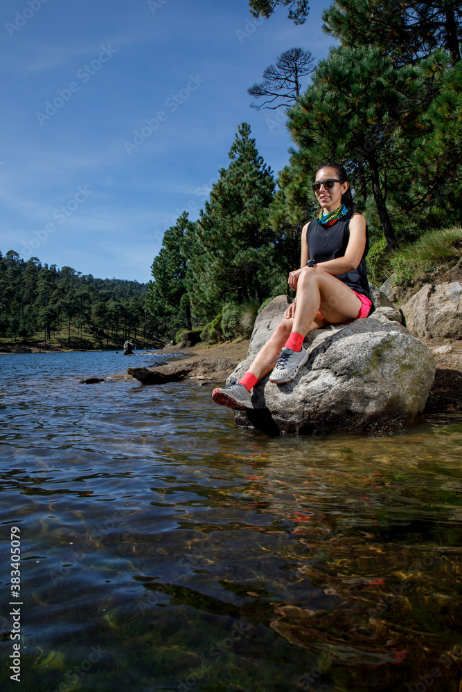 Atleta femenino descansando sobre una roca a la orilla de un lago, después de correr en el bosque