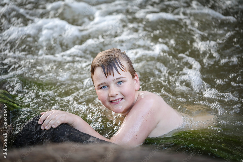 Obraz premium Boy swimming in river at dusk holding onto edge looking up at camera. Moody image with rich tones