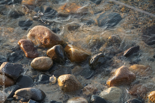 Rocks and pebbles sitting underwater on a sandy beach, during golden hour