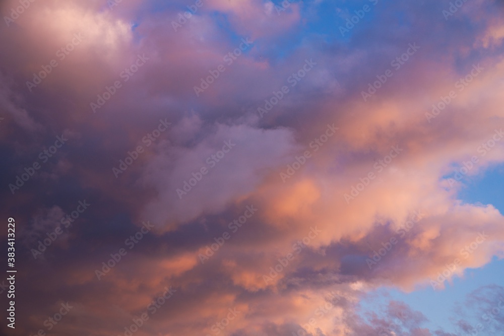 This beautiful image shows fluffy clouds glowing in shades of pink and orange clouds as they move through a blue early sunset sky.