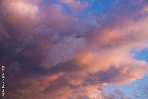 This beautiful image shows fluffy clouds glowing in shades of pink and orange clouds as they move through a blue early sunset sky.