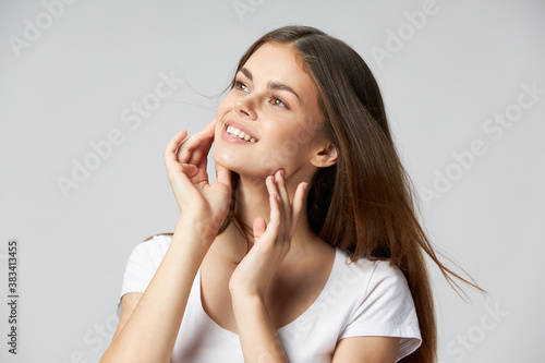 The woman smiles and touches her face with her hands on a light background 