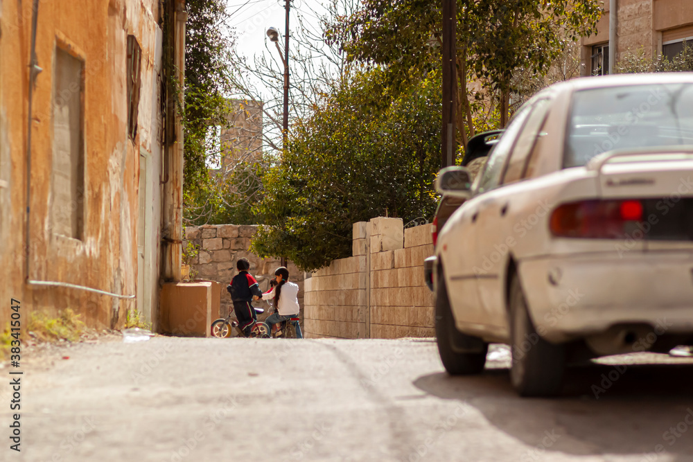 Despite cars using the road, Kids are playing and riding their bikes on a narrow street in an old and poor district of Hama which causes safety concerns.