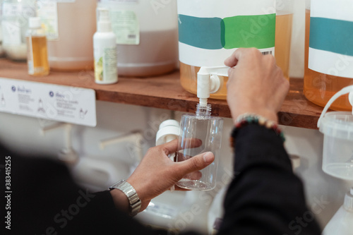Man using dispencer in eco shop putting liquid in plastic bottle.