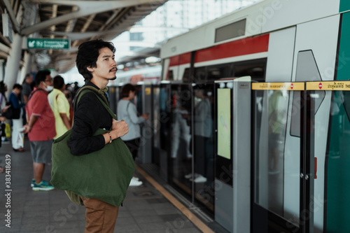 Asian man waiting for a train on platform.