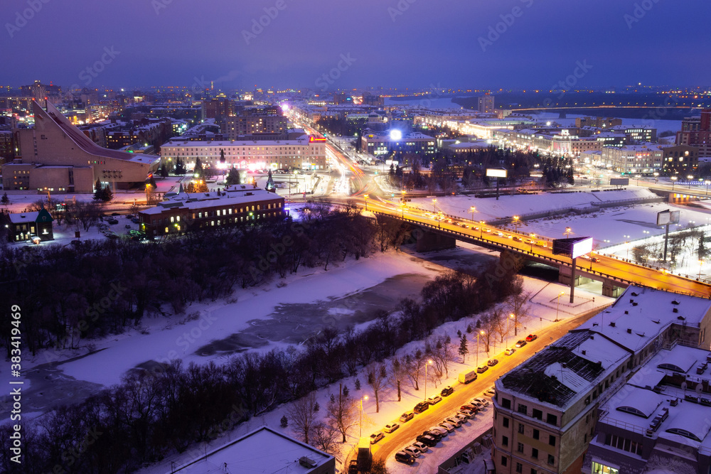Musical Theater across the Omka River. Komsomolsky bridge and Marx street that goes into the distance on a winter evening in Omsk