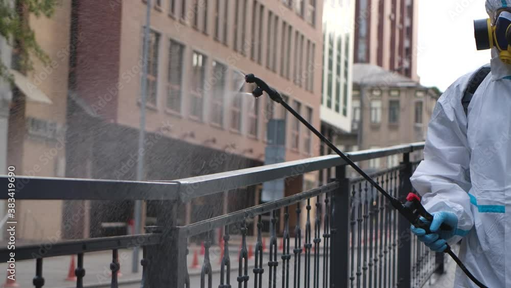 A working man in a white protective suit and a respirator disinfects, sprays chemicals on the surface of the railing from the coronavirus. Pressure washer close up. Slow motion. A working man in a white protective suit and a respirator disinfects, sprays chemicals on the surface of the railing from the coronavirus. Pressure washer close up. Slow motion.