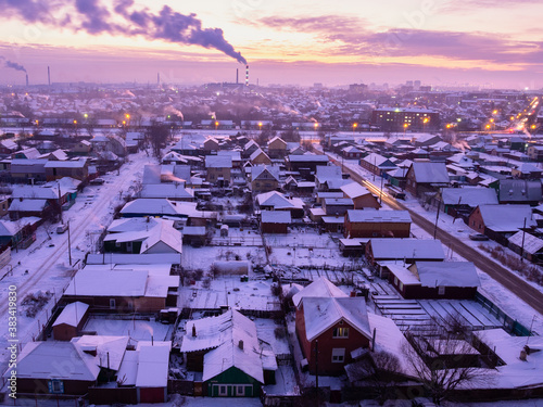 Private houses on the streets 13 and 14 workers in Omsk. Railroad and factory smoking chimney at sunset in winter.