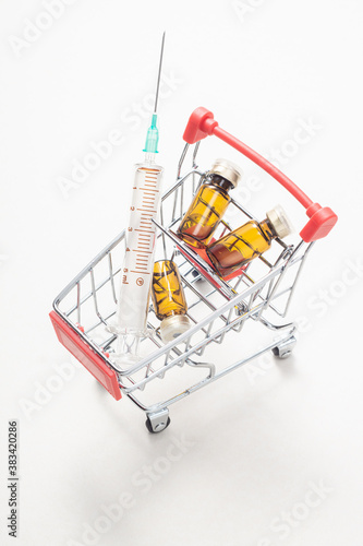 Vaccine vial and glass syringe on a mini shopping trolley on light background