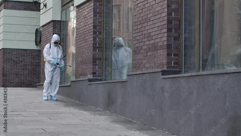 A virologist in a protective suit disinfects the surface, sprays liquid chemicals near the business center. Sanitary measures against coronavirus in public places. Slow motion. A virologist in a protective suit disinfects the surface, sprays liquid chemicals near the business center. Sanitary measures against coronavirus in public places. Slow motion.