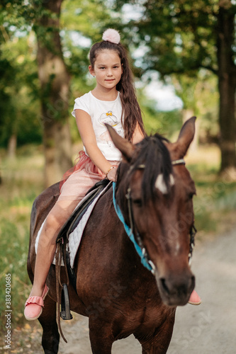 Little blonde girl with long hair rides a horse in the park at sunset in autumn. Autumn horse ride. Friendship of a girl and a horse.