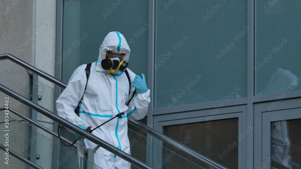 Man in protective suit disinfects street with an antiseptic sprayer. Surface treatment due to coronavirus disease. Virus pandemic and protection concepts. Close up. Slow motion. Man in protective suit disinfects street with an antiseptic sprayer. Surface treatment due to coronavirus disease. Virus pandemic and protection concepts. Close up. Slow motion.