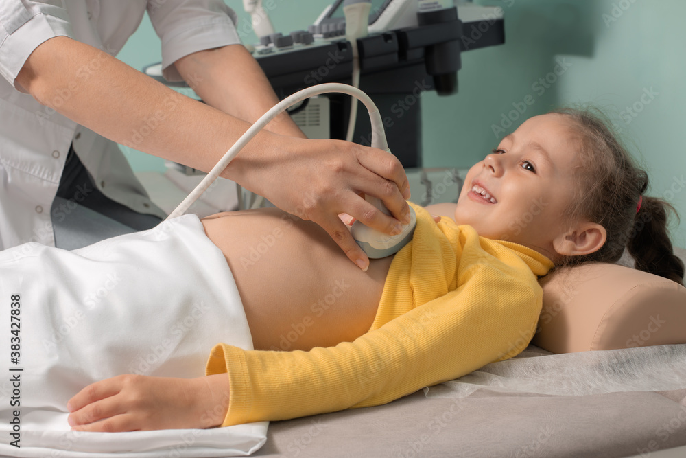 Doctor making abdominal ultrasound for child girl using scanner machine, side view. Woman runs ultrasound sensor over patient tummy looking at screen. Diagnostic examination of internal organs. Doctor making abdominal ultrasound for child girl using scanner machine, side view. Woman runs ultrasound sensor over patient tummy looking at screen. Diagnostic examination of internal organs.