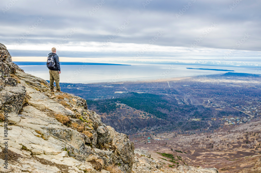 Adventurous man standing on the side of a mountain looking at the open landscape on a cloudy day.