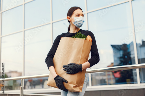 Girl in a medical mask. Woman holds a bag of groceries during an epidemic. The concept of food during quarantine. Coromavirus theme. photo