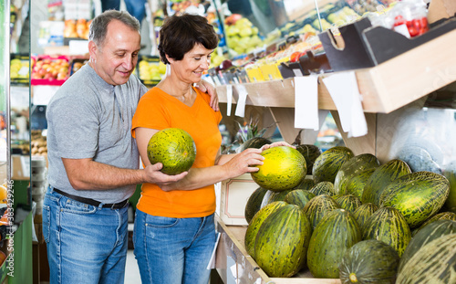 Nice man and his wife are choosing ripe melon in the fruit store