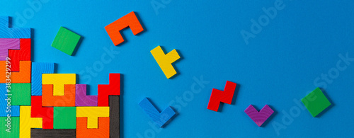 Different colorful shapes wooden puzzle blocks on light blue background. Geometric shapes in different colors, top view, copy space