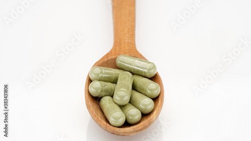 superfoods capsule moringa or spirulina in wooden spoon on white background