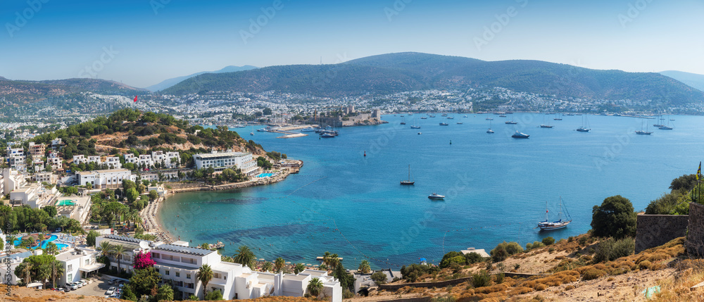 Fototapeta premium Panorama of Bodrum coastline with harbor and ancient fortress. Seascape with sailboats and luxury yachts in harbor on the Aegean sea in Bodrum, Turkey.