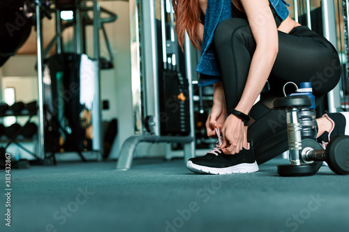 woman's hands tying shoelaces on sport sneakers in gym. dumbbell and water bottle on the ground around the sport girl. © Charnchai saeheng