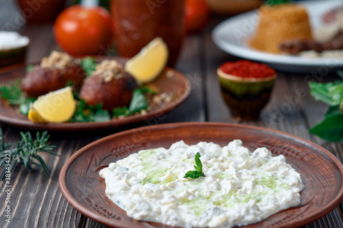 Ali nazik meze, a traditional Turkish dish of yoghurt and eggplant puree topped with a mint leaf. Side dish for kebab in a clay plate on a wooden background. Close-up, table setting.