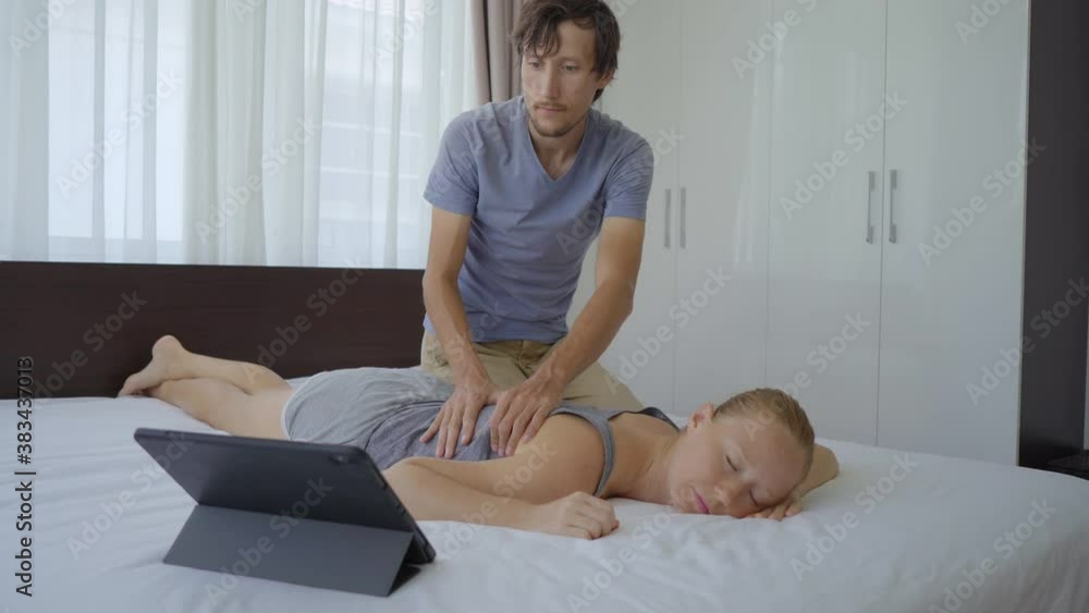 A young couple in the bedroom. Man learns how to perform a body massage for a woman by watching an online education video on a tablet. Online education concept. They stay at home because of the Covid A young couple in the bedroom. Man learns how to perform a body massage for a woman by watching an online education video on a tablet. Online education concept. They stay at home because of the Covid