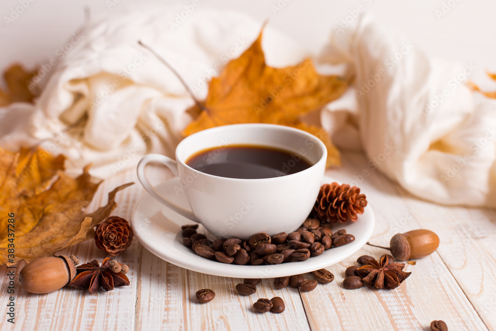 White scarf, a cup of coffee with scattered coffee beans, dry yellow leaves on a wooden table. Autumn mood, copy space.
