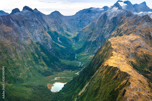 Amazing aerial view of yellow color mountain range, lake in the valley, forest on the scenic flight from Milford Sound to Queenstown through Mount Aspiring and Fiordland National Park, New Zealand