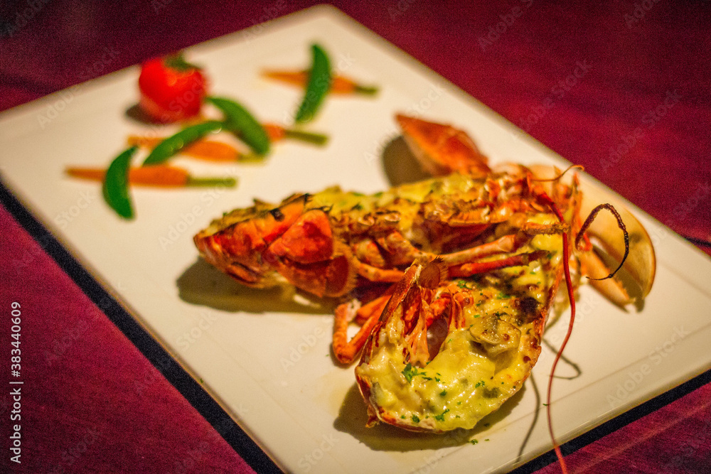 a whole grilled lobster with a tomato, snow peas and baby carrots on the side a whole grilled lobster with a tomato, snow peas and baby carrots on the side