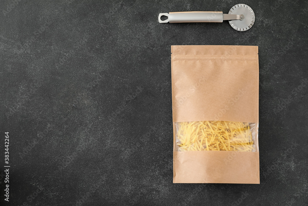 Paper bag with pasta and pizza cutter on dark background