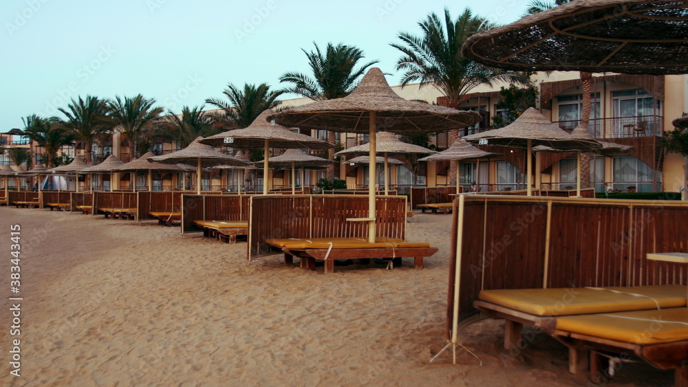 Cane umbrellas and sunbeds on sunset beach. Resort parasols on sky background.