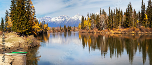 Panoramic view on the calm Irkut River in the foothill valley on a sunny autumn day. In the distance the snowy peaks of the Eastern Sayan Mountains. Siberia, Baikal region, Buryatia, Tunka valley