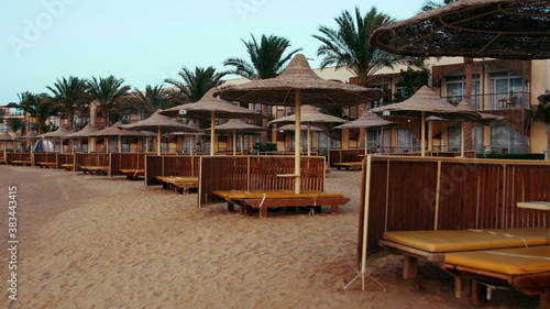 Cane umbrellas and sunbeds on sunset beach. Resort parasols on sky background.