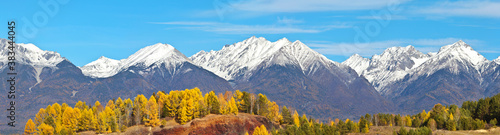 A panoramic view of the snow-capped peaks of the Eastern Sayan mountain range on a sunny autumn day. Siberia, Buryatia, Tunka foothill valley. Beautiful autumn landscape. Natural background