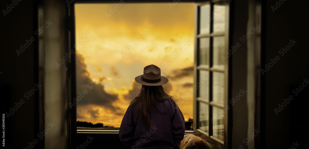 a silhouette of a girl with a hat looking at admiring outdoor sunset on the window.
