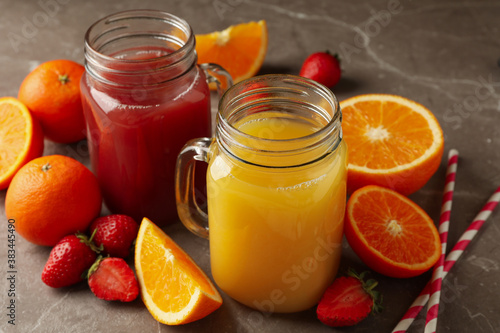 Glass jars with strawberry and orange juices on gray background