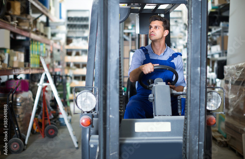 Salesman in uniform is sitting in loader near shelves in the building store.