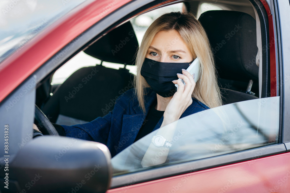 Young girl in a black mask sitting in a car and talking on the phone, protective mask against coronavirus