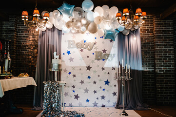 Birthday Cake on a background blue, white and silver balloons, brick wall. Baby shower party, decor. Cake with figure carriage for a boy. Copy space. Celebration baptism concept.