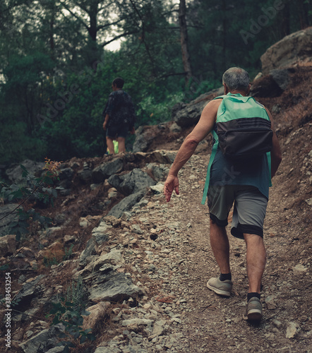 Senior man climbing up the path in the forrest. Image of a hiker from the back in the nature. photo