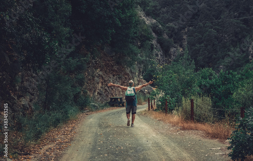 Senior man in the middle of the road in the forrest. Image of a hiker from the back in the nature with hands open. photo
