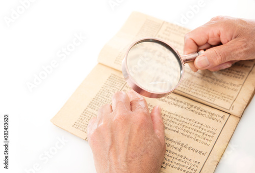 Schilderij op canvas An old man is holding a magnifying glass in hand to look up on an old yellowed b